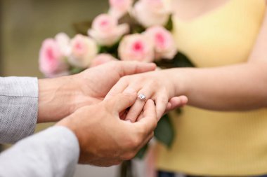 Evlilik teklifi yapıyor. Bir adam dışarıda kız arkadaşının parmağına nişan yüzüğü takıyor, yakın plan.