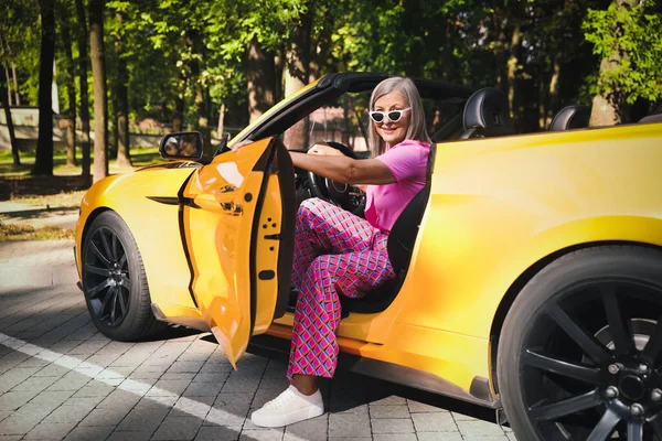 Güneş gözlüklü şık bir son sınıf öğrencisi modern Cabriolet 'ten dışarı çıkıyor.