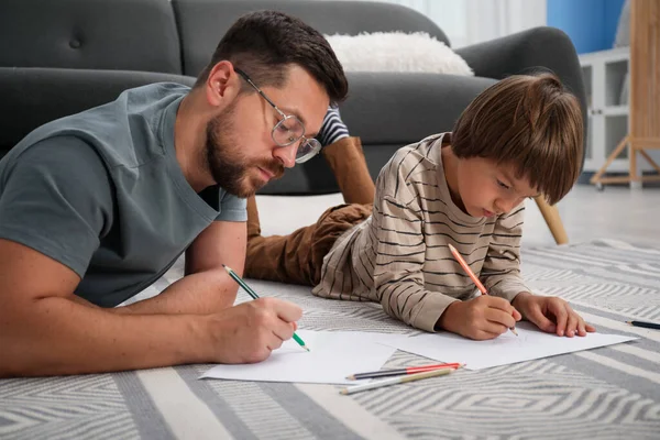 Baba ve oğul evde yerde birlikte çiziyorlar.