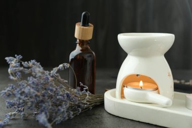 Aroma lambası yanan mum, damlatan ve lavanta gri desenli masa üzerinde siyah arkaplan, yakın plan