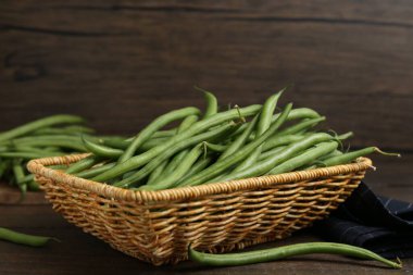 Hasır sepetin içindeki taze yeşil fasulye kabukları ahşap masanın üzerinde, yakın plan.