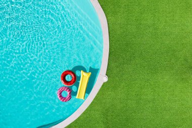 Yüzme havuzunda yüzen şişme halkalar ve şilte yeşil çimlerle çevrili.