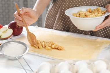 Elmalı turta yapıyorum. Mutfaktaki masada meyveleri hamura koyan kadın, yakın plan.