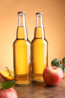 Cam şişelerde lezzetli elma şarabı ve ahşap masada portakal eğimli arka planda elmalar.