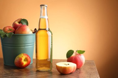 Cam şişede nefis elma şarabı ve portakal renkli arka planda ahşap masada elmalar. Metin için boşluk