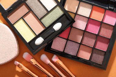 Göz farı paletleri ve fırçalar turuncu arka planda, manzaranın üstünde. Makyaj kozmetikleri