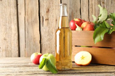 Cam şişede nefis elma şarabı ve tahta masada elmalar.