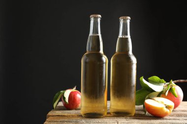 Cam şişelerde nefis elma şarabı ve ahşap masada koyu gri arka planda elmalar. Metin için boşluk