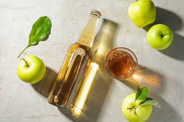 Şişede nefis elma şarabı, yeşil yapraklı cam ve elmalar gri desenli masa, düz uzanmış