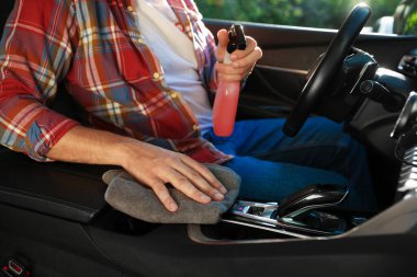 Salonda araba merkezi konsolunu gri mikrofiber bezle silen adam, yakın plan.