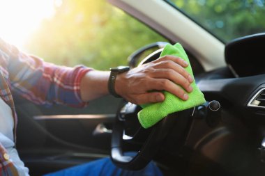 Araba kuaföründe direksiyonu yeşil mikrofiber bezle silen adam, yakın plan.