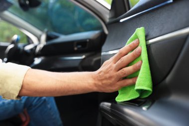Salondaki yeşil mikrofiber bezle araba kapısını silen adam, yakın plan.