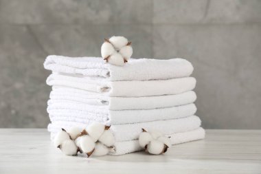 Gri duvara karşı açık ahşap masada katlanmış havlular ve pamuk çiçekleri yığını.