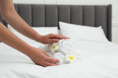 Kadın beyaz havlu yığını ve Plumeria çiçeklerini yatağın içine koyuyor, yakın plan.