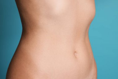 Açık mavi arka planda düz göbekli genç kadın, yakın plan.