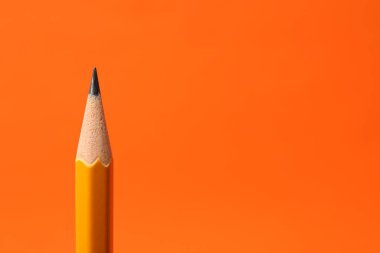 Turuncu arka planda keskin bir grafit kalem, yakın plan. Metin için boşluk