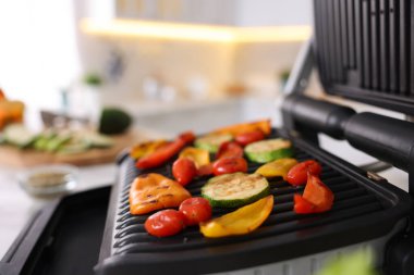 Mutfaktaki beyaz masada farklı sebzelerle elektrikli ızgara, yakın plan.