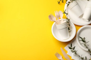 Tek kullanımlık sofra takımı ve okaliptüs dalları sarı arka planda, düz yerde. Metin için boşluk