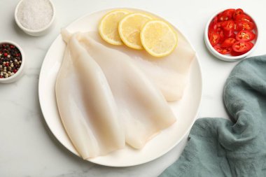 Beyaz mermer masa üzerinde limon ve baharatlı çiğ kalamar parçaları, düz yatıyordu.