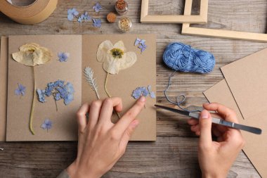 Ahşap masa, üst manzara, kuru çiçekleri deftere koyan kadın.