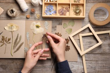 Ahşap masa, üst manzara, kuru çiçekleri deftere koyan kadın.