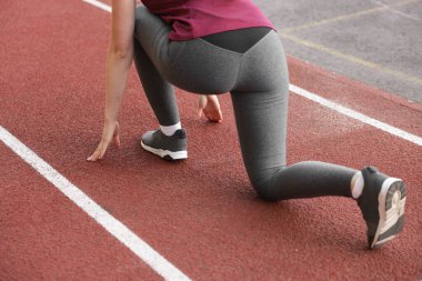 Stadyumda koşmak için başlangıç pozisyonunda olan kadın, yakın plan.