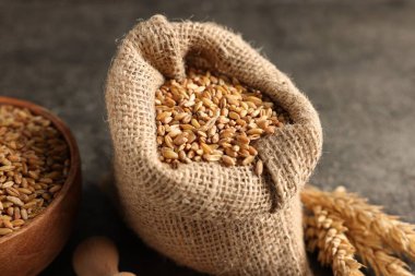 Çuvaldaki buğday taneleri ve gri masadaki çiviler, yakın plan.