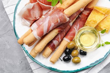 Grissini ekmekleri jambon, peynir, zeytin ve bal ile gri masada, üst görünümde.