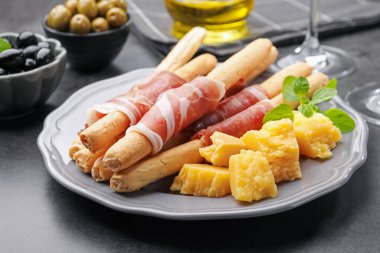 Grissini ekmeği jambonlu, peynirli ve zeytinli, gri masada, yakın plan.