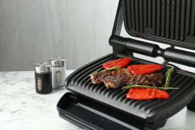 Elektrikli ızgara biftek, dolmalık biber ve biberiye beyaz mermer masada, yakın plan. Metin için boşluk