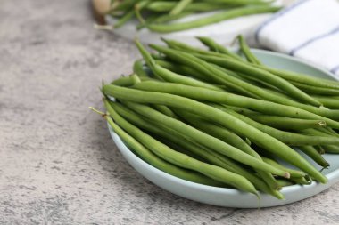 Fresh green bean pods on grey textured table, closeup