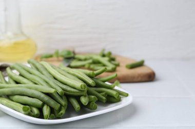 Cut green bean pods on white tiled table, closeup. Space for text
