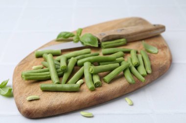 Cut green bean pods and knife on white tiled table, closeup