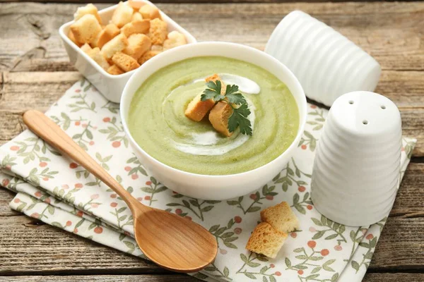 Tasty broccoli cream soup with croutons served on wooden table, closeup