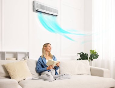 Evdeki kanepede kitap okuyan bir kadın. Klima içeride rahat bir sıcaklık sağlıyor.