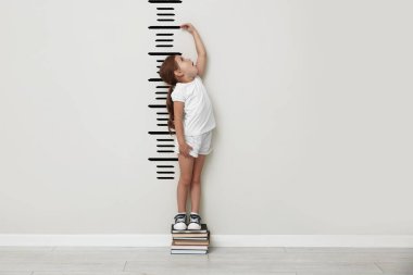 Kitaplarda boyunu beyaz duvarla ölçen sevimli küçük bir kız.