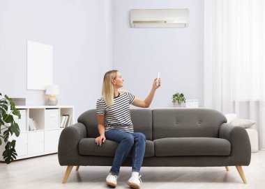 Evdeki koltukta uzaktan kumandayla klima kullanan bir kadın.