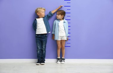 Sevimli küçük kız ve oğlan boylarını menekşe duvarla ölçüyorlar.