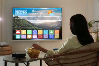 Akşam evde video projektörüyle televizyon izleyen bir kadın. Ekranda simge ve bilgi içeren menü