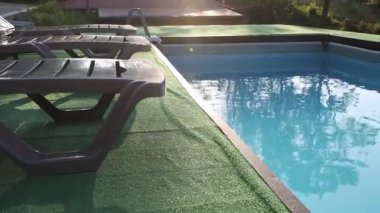 Dışarıdaki yüzme havuzunun yanındaki yapay çimenlerin üzerinde şişme halkalı boş güneş panelleri. Kamera sağa hareket ediyor