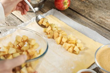 Elmalı turta yapıyorum. Ahşap masada meyveleri hamura koyan kadın, yakın plan.
