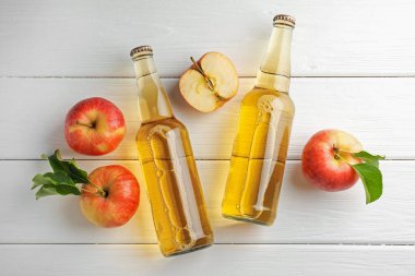 Cam şişelerde nefis elma şarabı ve beyaz ahşap masada elmalar.