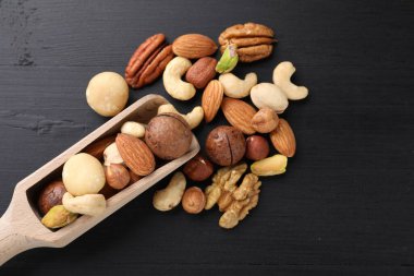 Mix of different nuts and scoop on black wooden table, flat lay. Space for text