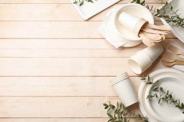 Tek kullanımlık sofra takımı ve okaliptüs dalları açık ahşap masada, düz yerde. Metin için boşluk