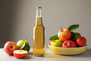 Cam şişede nefis elma şarabı ve arka planda gri masada elmalar