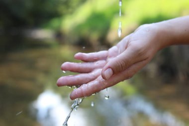 Su kavramını sakla. Nehrin kenarında, temiz suyun altında elini tutan kadın, yakın plan.