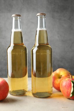 Cam şişelerde lezzetli elma şarabı ve gri arka planda elmalar.