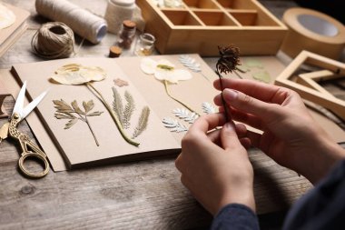 Ahşap masadaki kuru çiçekleri deftere koyan kadın, yakın plan.