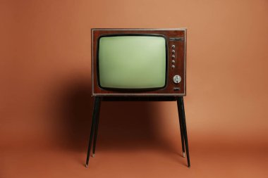 Retro TV set on stand against brown background. Used stuff