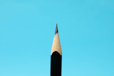 One sharp graphite pencil on light blue background, closeup